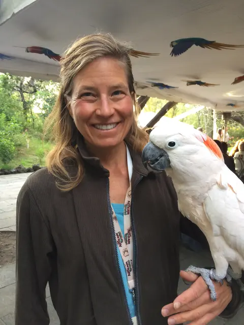 A smiling woman with a white cockatoo perched on her shoulder