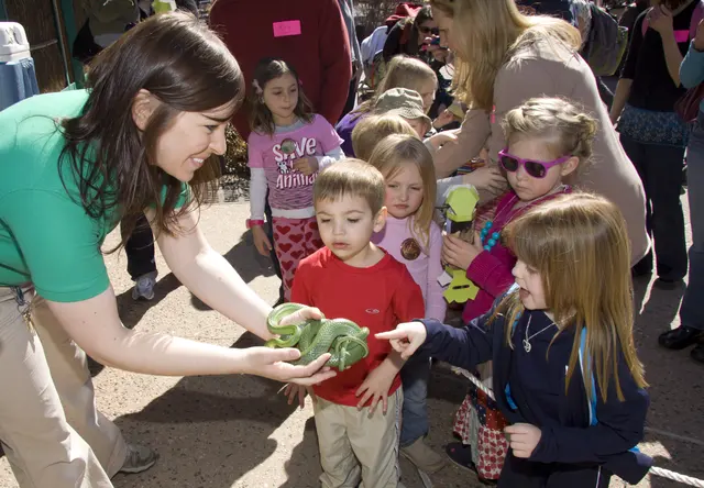 An educator showing a small animal to a crowd of excited kids